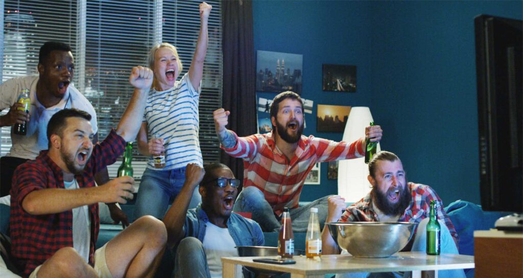 6 Bekannte sitzen jubelnd vor dem Fernseher